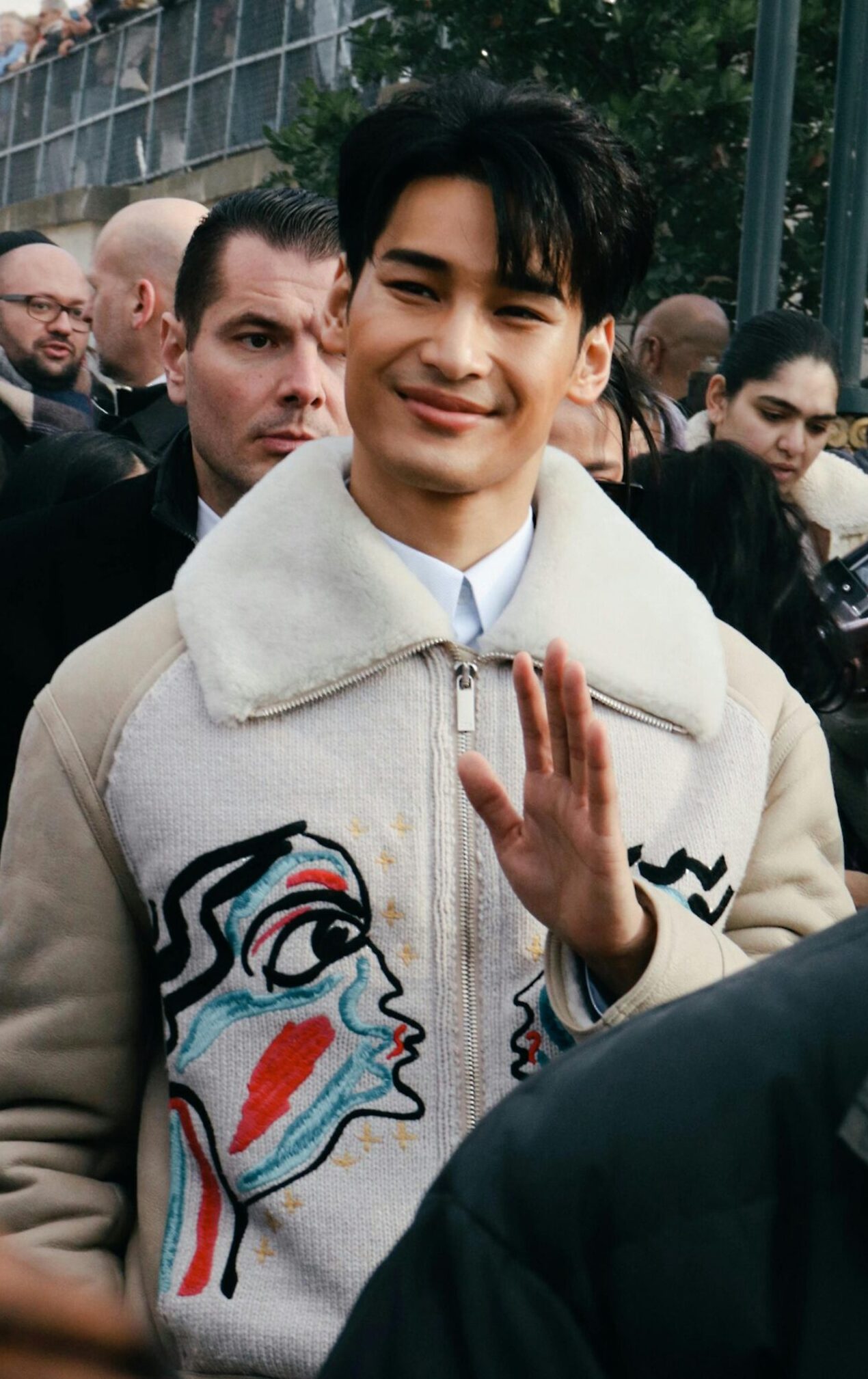 Smiling man among a crowd on a lively Paris street, capturing modern fashion and public event atmosphere.